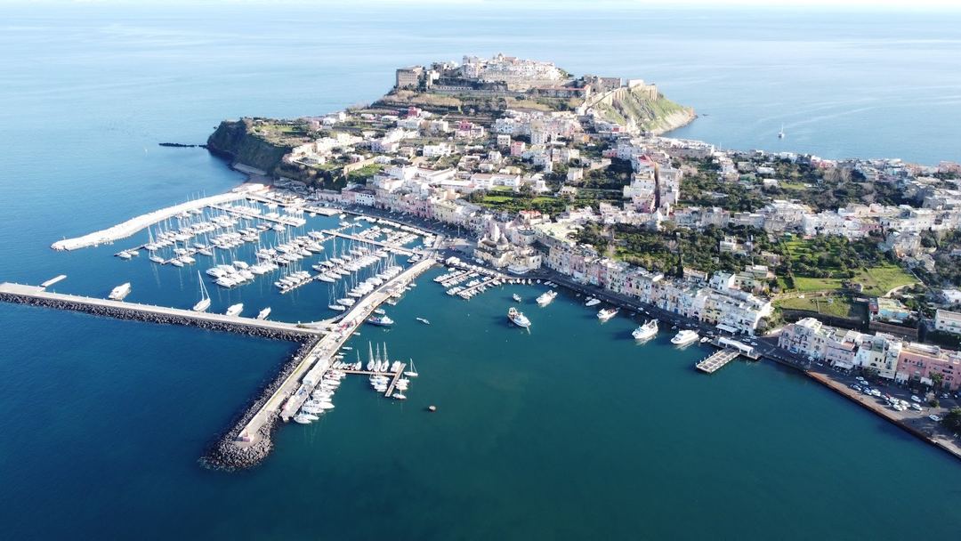 Aerial view of Procida island showing the marina, historic architecture, and fortress overlooking the Mediterranean coast.